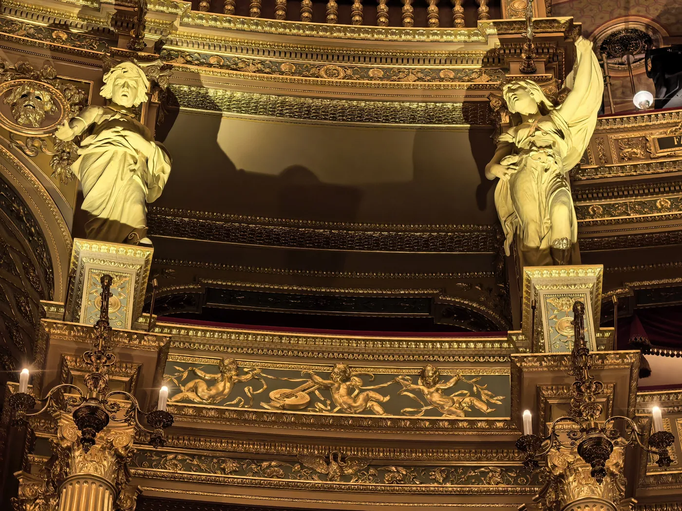 Dos figuras doradas que flanquean un palco con balaustrada dorada en la sala