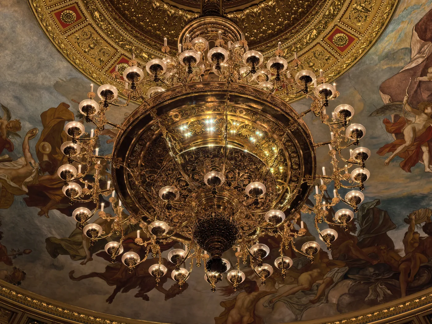 Un candelabro dorado visto desde abajo contra el techo pintado de la sala
