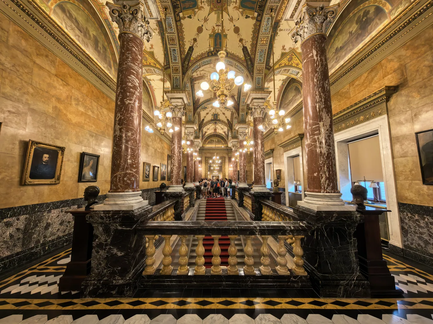Un largo salón de columnas de mármol, retratos enmarcados y candelabros en el interior de la Ópera