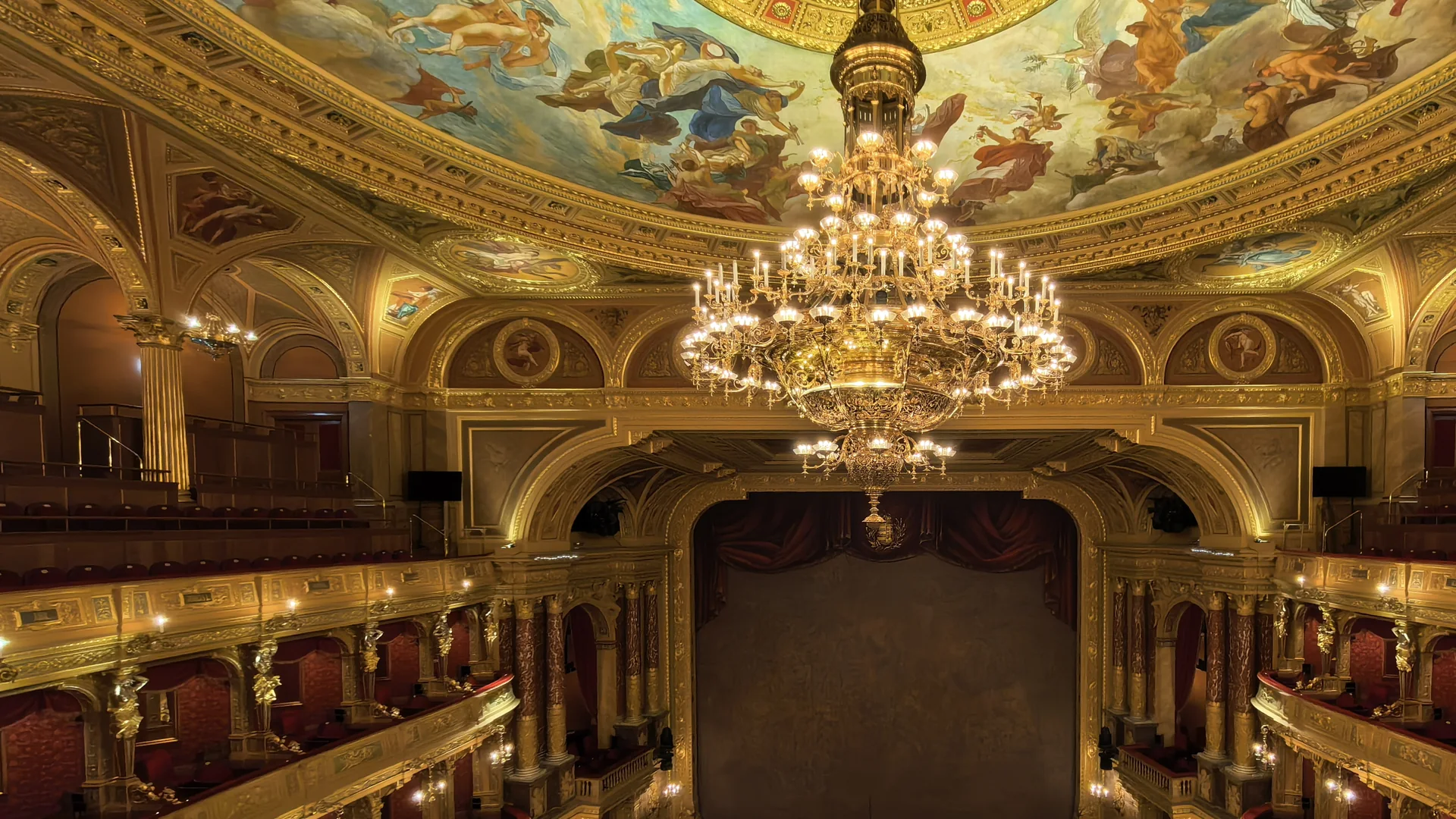 El auditorio de la Ópera Estatal Húngara, con una lámpara dorada colgando bajo el techo pintado frente al escenario